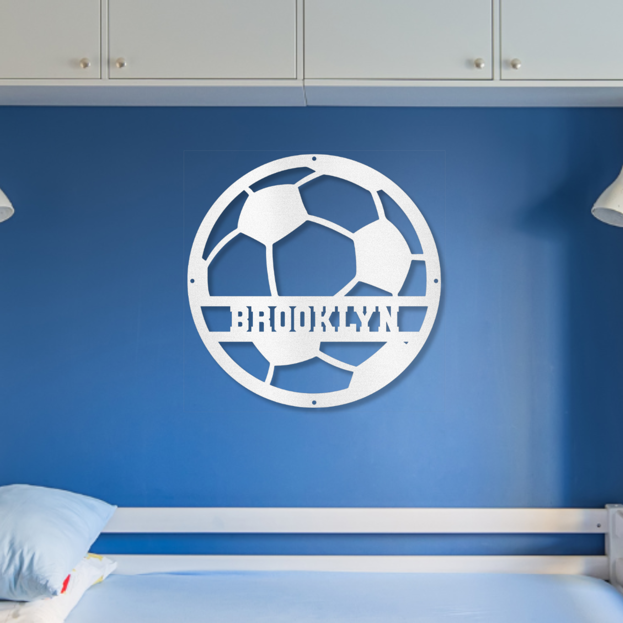 Children's bedroom with a bed, shelves, and a blue wall with a white soccer ball metal wall art design with the name
"Brooklyn".